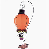 Back or rear Full-length view of the 2025 Katherines Collection Halloween Ghoulish Hot Air Balloon with glowing tea light, pumpkin face wearing a top hat with plaid fabric trim, witch and cat in basket and bats flying at the base of the stand