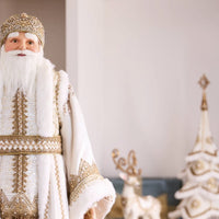 Man in a traditional Russian Christmas costume standing in a decorated room with a Christmas tree and gifts.
