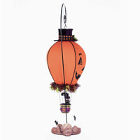 Right side Full-length view of the 2025 Katherines Collection Halloween Ghoulish Hot Air Balloon with glowing tea light, pumpkin face wearing a top hat with plaid fabric trim, witch and cat in basket and bats flying at the base