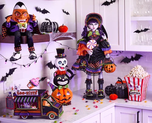Halloween-themed display with dolls, pumpkins, and popcorn on a kitchen counter.