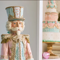 Decorative nutcracker figure with pastel colors next to a Christmas-themed cake.