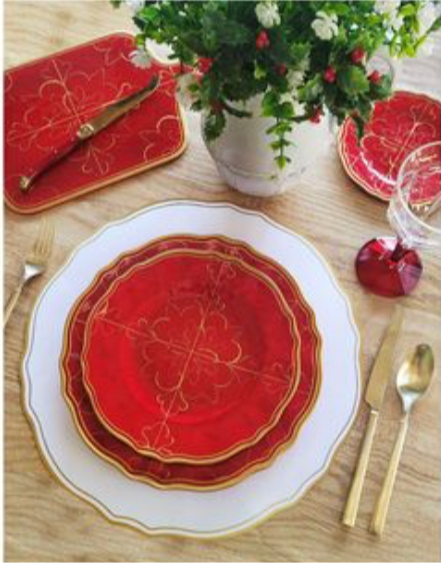 Decorative red Le Cadeaux Bellini holiday salad plate with gold accents on a table setting with a vase of flowers and cutlery.