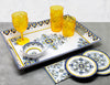 Decorative ceramic tray with plates, bowls, and yellow glasses on a gray surface.