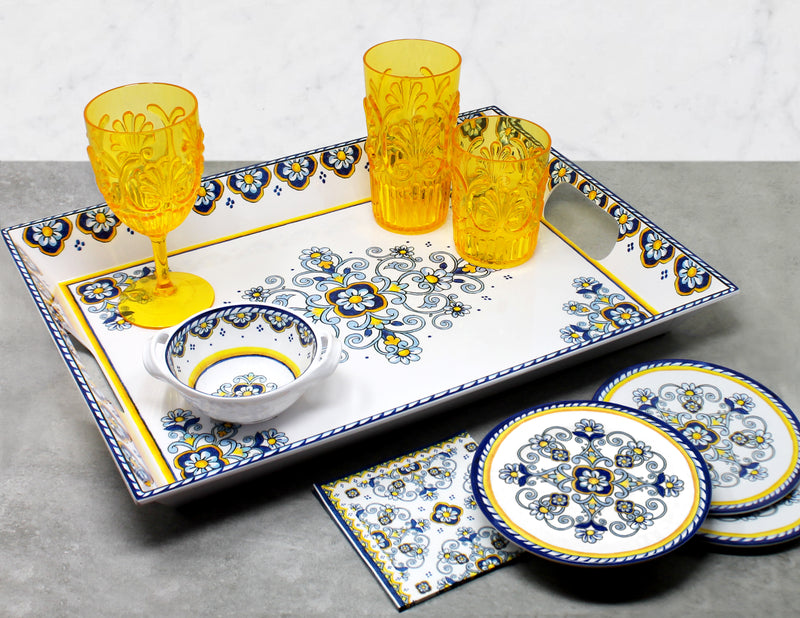 Decorative ceramic tray with plates, bowls, and yellow glasses on a gray surface.