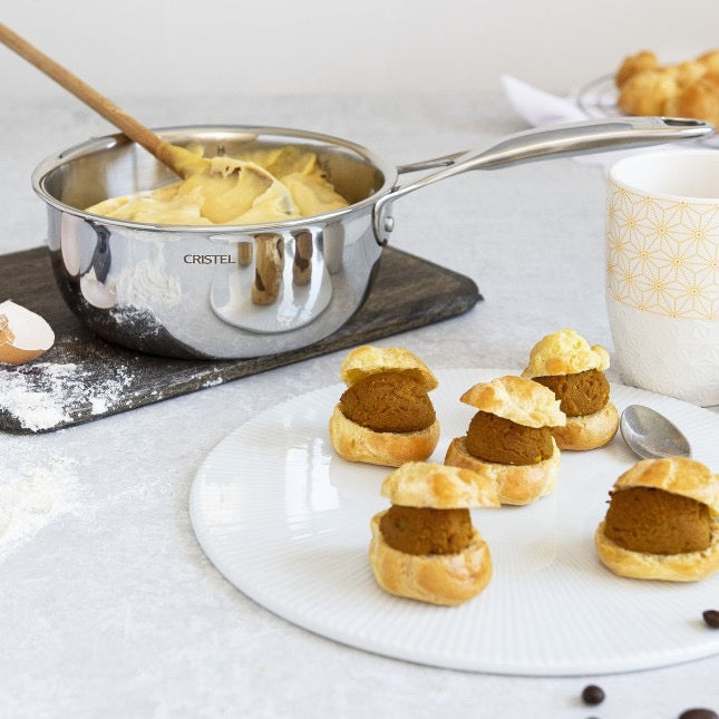 Cristel pot with fillings for small pastries with a filling on a white surface  and a container of cream.