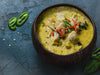 Bowl of yellow curry with chicken and vegetables on a dark surface by Verve Culture 