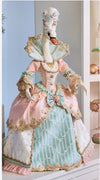Decorative figure in a pastel-colored gown with gold accents on a white surface.