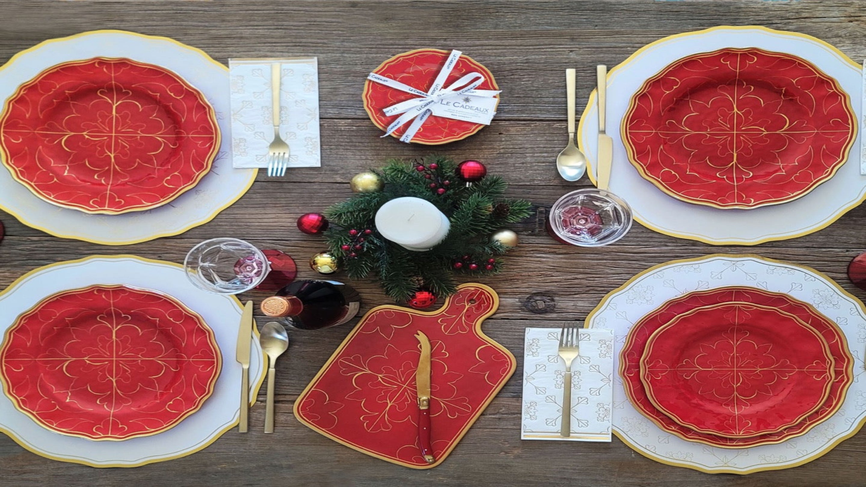 Elegant Christmas table setting with red and gold plates, silverware, and festive decor on a wooden table.