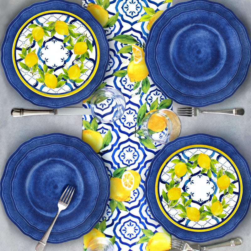 Set of le cadeaux Campania Blue blue dinner and salad plates with le Cadeaux Palermo lemon design salad plates on a matching Le Cadeaux Palermo tablecloth, Santorini Clear tumblers arranged on a gray surface.