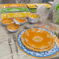 Le Cadeaux Paloma Yellow Orange Green Dining table set with colorful plates, bowls, and cutlery on a white tablecloth.