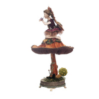 left side view of detailed fairy figurine perched on a sculpted mushroom, dressed in elegant fabrics and sparkling jewels.