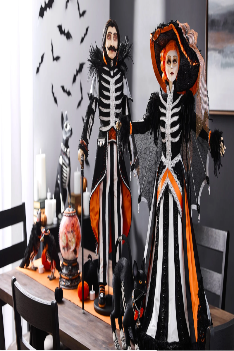 A promotional banner for 'The Macabre Family' featuring a collection of Halloween dolls. The left side has a dark brown text block with white text, while the right side shows three detailed dolls: a skeleton mother with a black and white striped dress, a skeleton father in a black suit, and a skeleton child in a black and orange dress, all set in a dark, spooky room with black bats flying in the background.