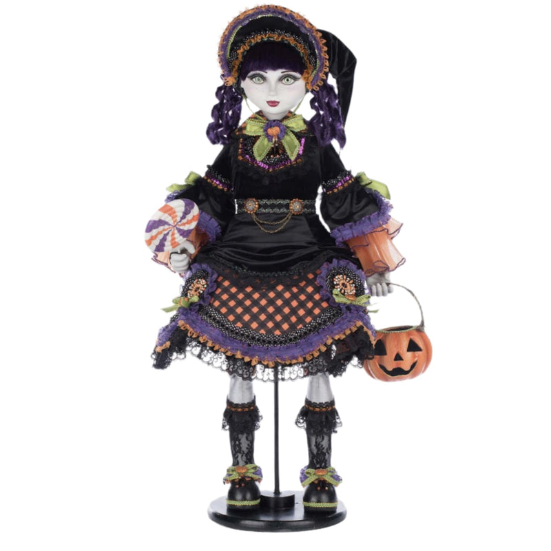 Halloween-themed doll in a black outfit with purple accents, holding a pumpkin bucket on a white background.