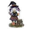 Front-facing view of Katherine's Collection Poppy Broomson Witch standing over her cauldron reading a spell book, with pumpkins at her feet in an orange and black buffalo plaid dress and jeweled accents. and black witches hat