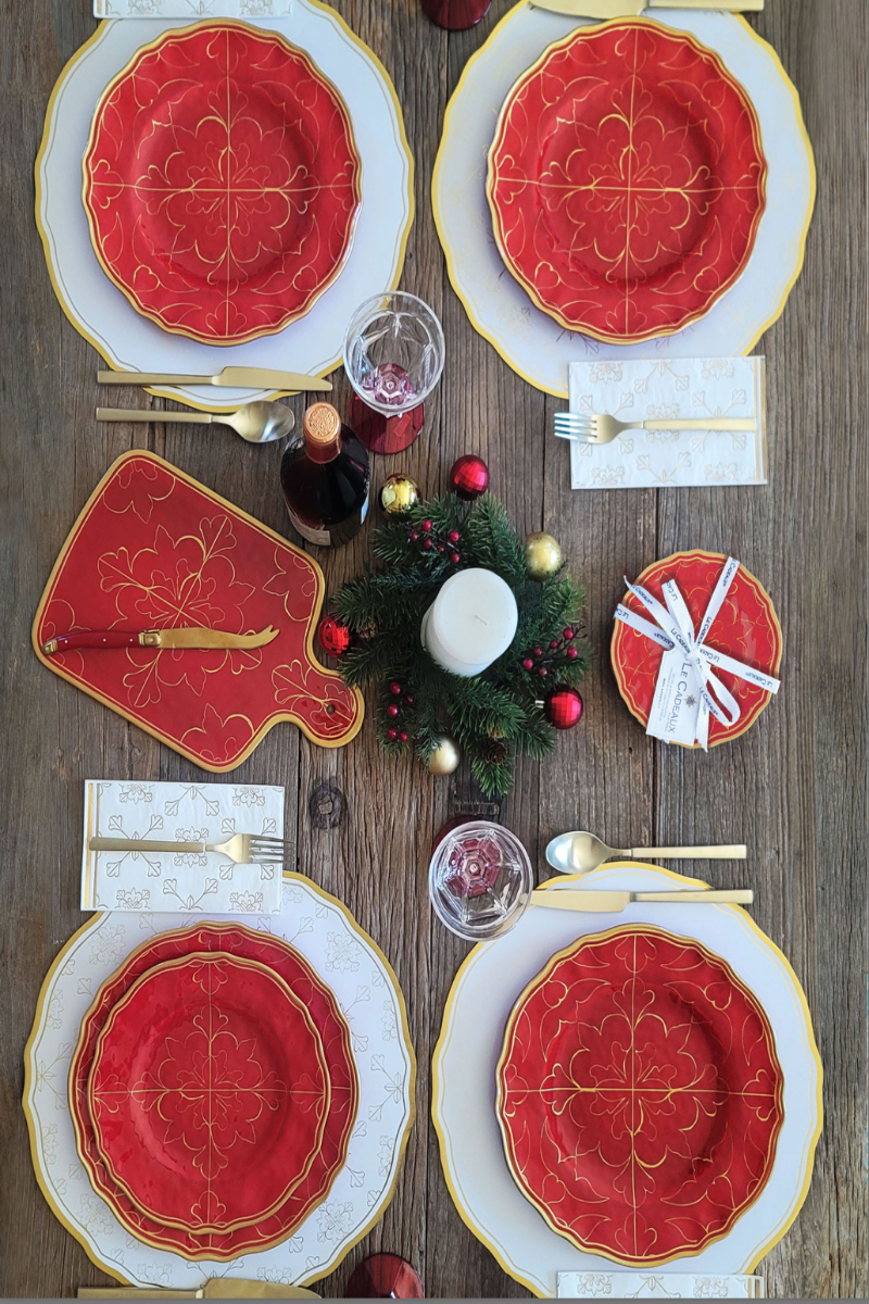 Elegant Christmas table setting with red and gold plates, silverware, and decorative elements on a wooden table.