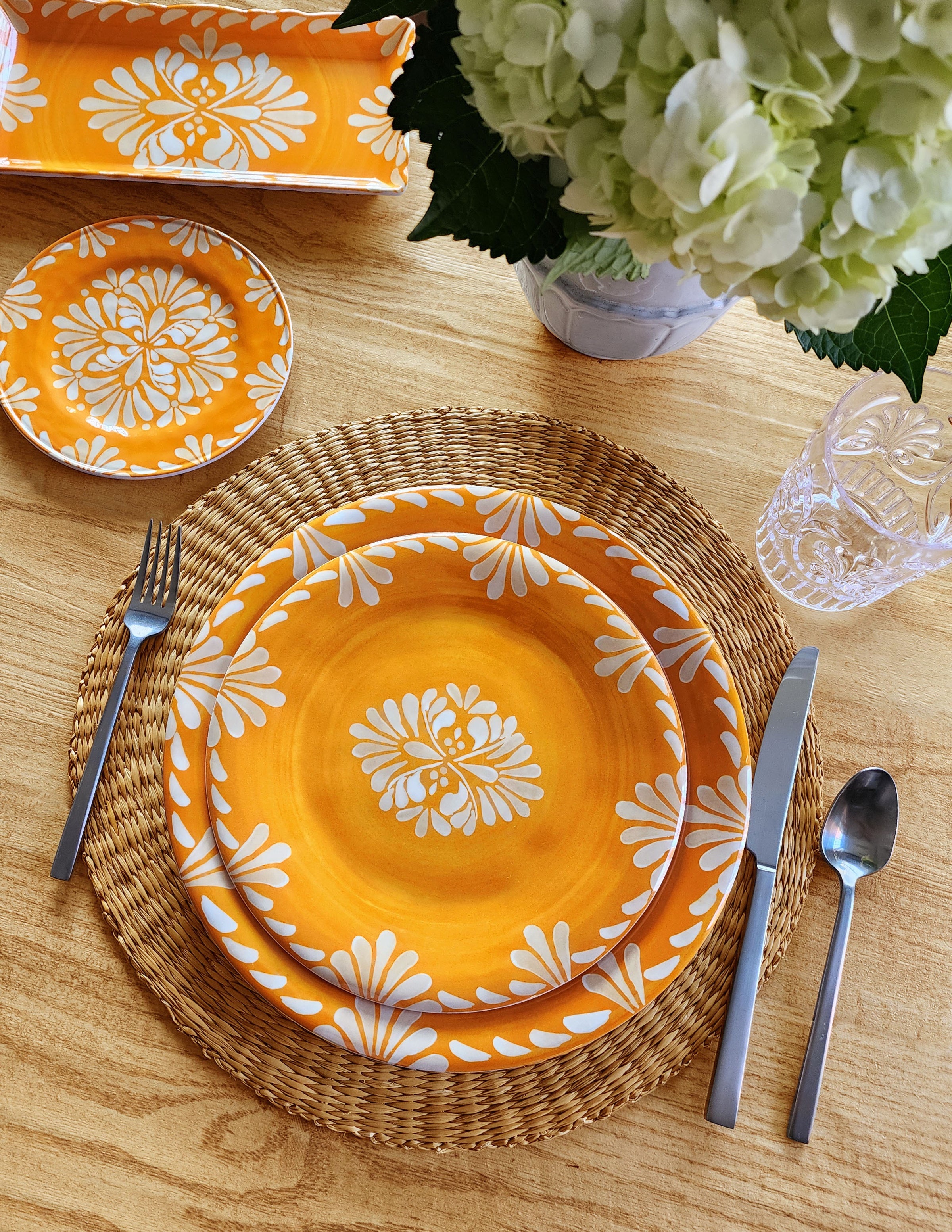 Le Cadedaux Paloma Orange plates with white floral patterns on a wooden table with silverware and flowers.
